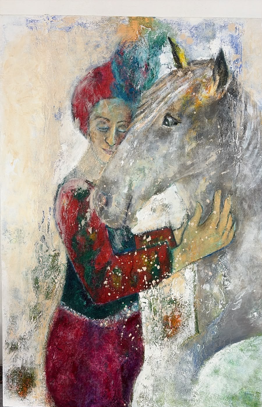 Painting by Claudia Artecura: a woman with closed eyes and a red and turquoise headdress embraces a grey horse, cheek to cheek, in soft cream, red and green tones.