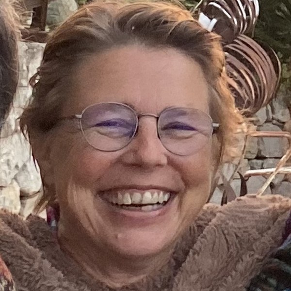 Portrait of Claudia Artecura laughing, round glasses and light brown hair, at a table outdoors at sunset in Ibiza.
