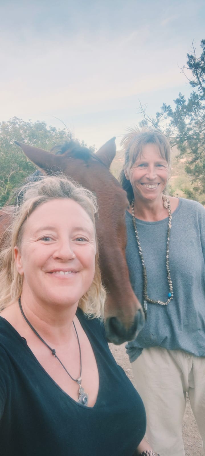 Joke en Marzena glimlachen samen, met Kashi Pushi, een bruin paard, tussen hen in; achter hen bomen en een avondlucht.