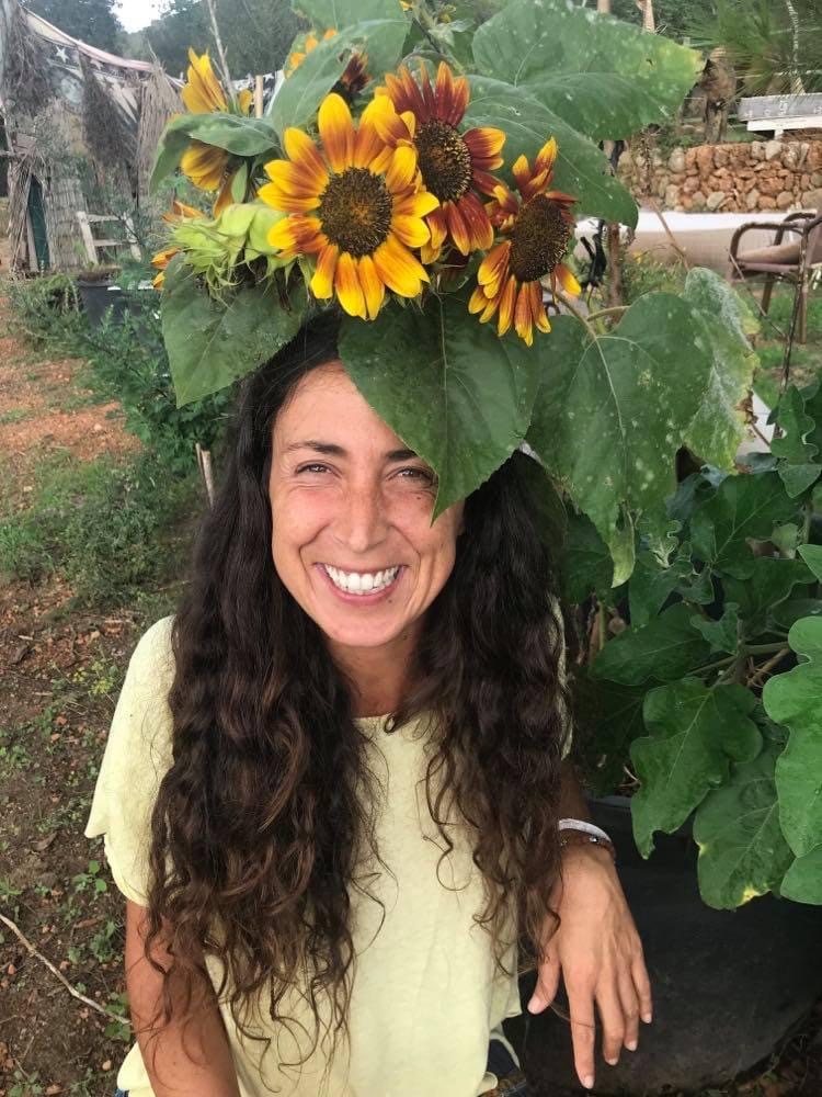 Shweta Aaliyah laughing, long dark curly hair, a crown of sunflowers and big leaves on her head, in a garden in Ibiza.